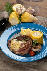 Grilled rib eye steak with vegetables and potato puree in butter sauce isolated on rustic wooden table