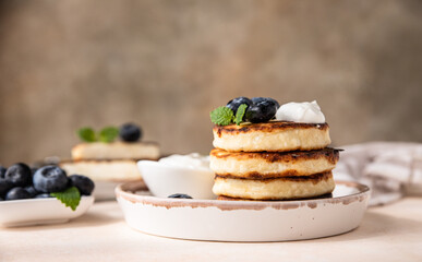 Fried cottage cheese pancakes or fritters with fresh blueberry and sour cream on a plate. Gluten free. Traditional breakfast of Ukrainian and Russian cuisine. 