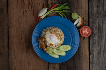 Top view of fried rice with egg on top, pork crackling and cucumber isolated on rustic wooden table