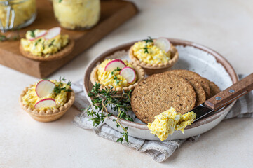 Tartlets with egg pate or salad and radish and thyme on light stone background. Egg dip in glass jar. 