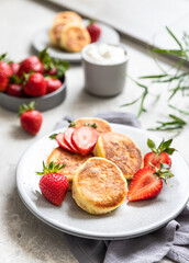 Cottage cheese pancakes or fritters with strawberry and natural yogurt on light grey stone background. Healthy breakfast or lunch. Syrniki.