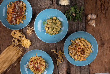 Top view variety of homemade prepared pasta isolated on wooden table. Penne aglio e olio prawn, spaghetti carbonara, fettuccini Bolognese and gnocchi pesto