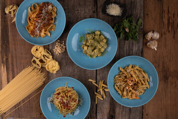 Top view variety of homemade prepared pasta isolated on wooden table. Penne aglio e olio prawn, spaghetti carbonara, fettuccini Bolognese and gnocchi pesto