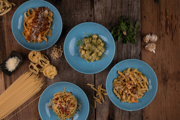 Top view variety of homemade prepared pasta isolated on wooden table. Penne aglio e olio prawn, spaghetti carbonara, fettuccini Bolognese and gnocchi pesto