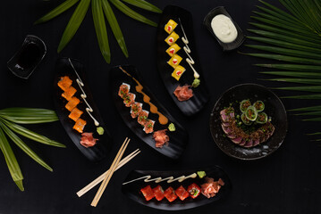 Top view mix of sushi, Japanese food over black table with tropical leaves