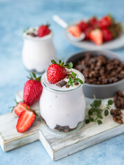 Healthy breakfast or dessert with natural yogurt, chocolate granola and strawberries, blue concrete background. 