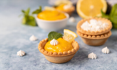 Mini tarts with lemon curd, mini meringue, lemon slices and mint on blue concrete background. 