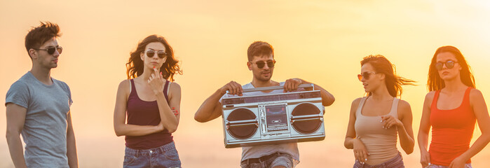 The five happy people stand with a boom box on the sunset background © realstock1