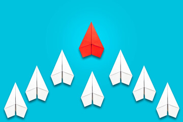 Red paper plane flying in front of a group of whites. Blue background. Copy space. Leadership concept, teamwork, personnel management. Business. Lifestyle.