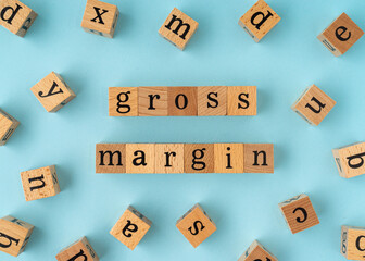 Gross Margin word on wooden block. Flat lay view on blue background.