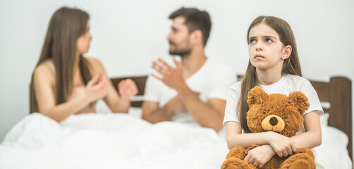 The girl with a soft toy sitting near the parents in the bed