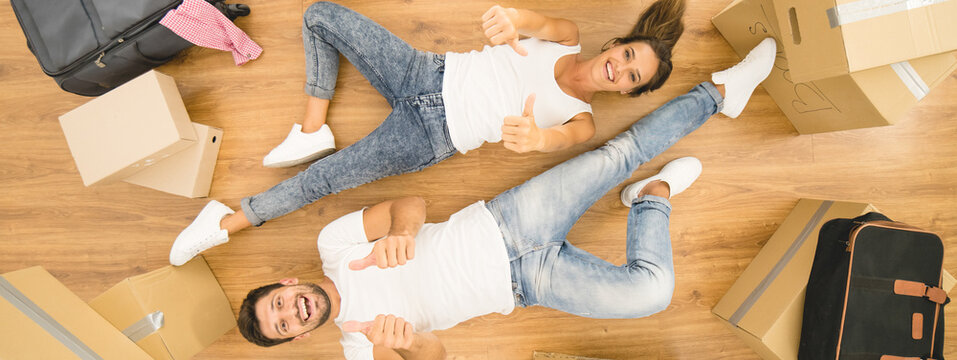The smile couple lay on the floor and thumb up near boxes. view from above