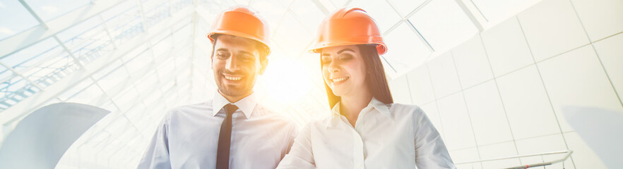 The man and woman in a helmets hold the project plan in the building