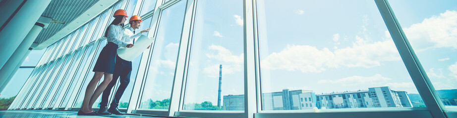 The man and woman in a helmets stand near the window and gesture
