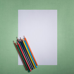 A blank white sheet and colored pencils for drawing on a plain textured background with space for copying and lettering.