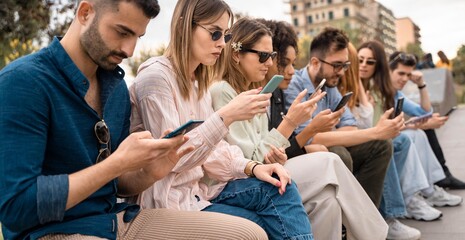 Group of young people surfing the internet watching social network contents sitting outdoors. Friends addicted from smartphones and people using tech concept.