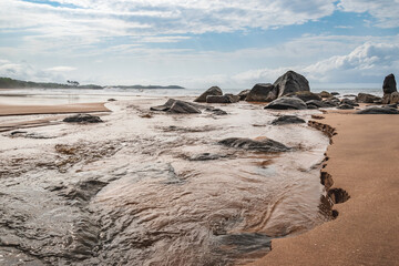 A lagoon that flows out by the sea with black stones lying on the coast of Axim Ghana West Africa