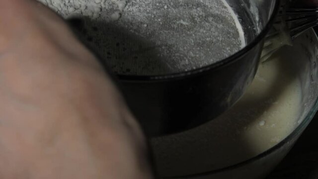 Skilled cook sifts flour over bowl with white pancakes dough holding sifter and whisk closeup. Concept restaurant nutrition