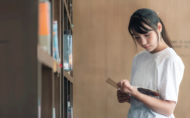 Beautiful asian student reading a book while standing in library.