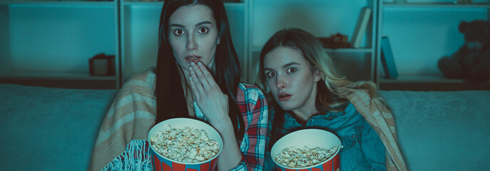 The two women with a popcorn watch a horror movie on the sofa