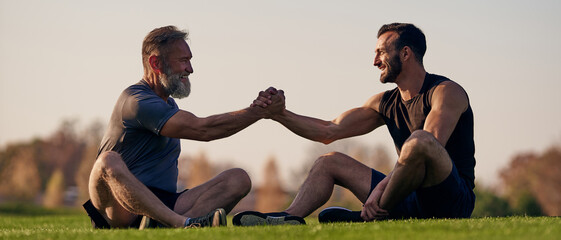 The two happy men sitting on the grass and greeting - obrazy, fototapety, plakaty