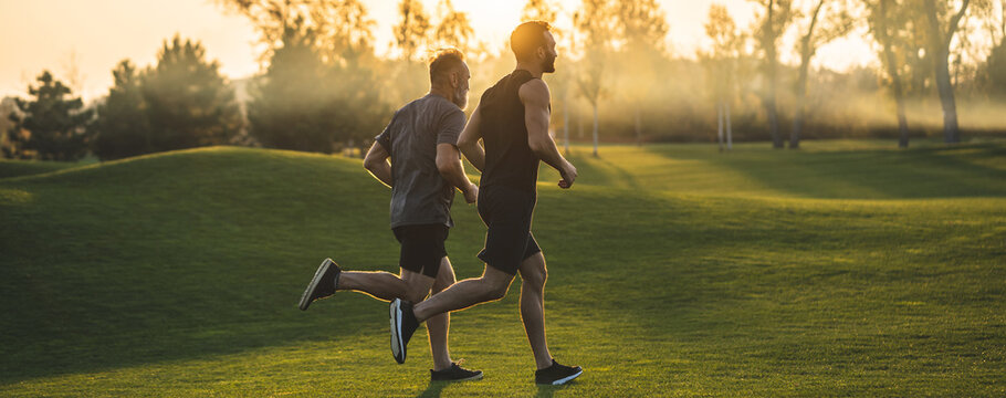 The two sportsmen running on the grass in the park on the sunny background