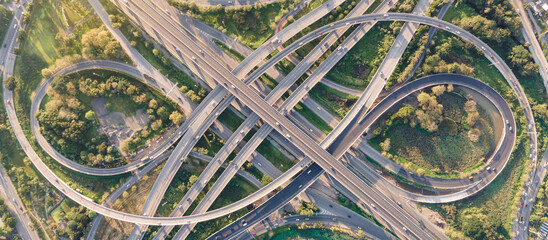 Aerial view of road interchange or highway intersection with busy urban traffic speeding on the road. Junction network of transportation taken by drone. - obrazy, fototapety, plakaty