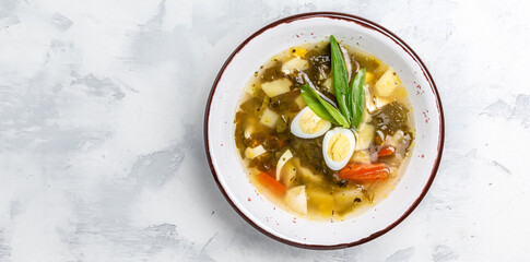 Green herb cream soup in the bowl. Sorrel soup with egg, potatoes, carrots, parsley. Long banner format. top view