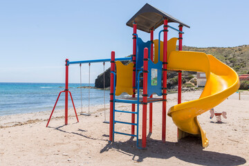 Children's playground with slide, swings and climbing area, located on the shore of the Spanish beach of Puntas de Calnegre. - obrazy, fototapety, plakaty