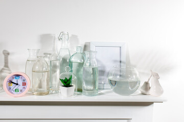 A set of water bottles of different shapes with a photo frame and a pot with artificial succulent is on the dresser