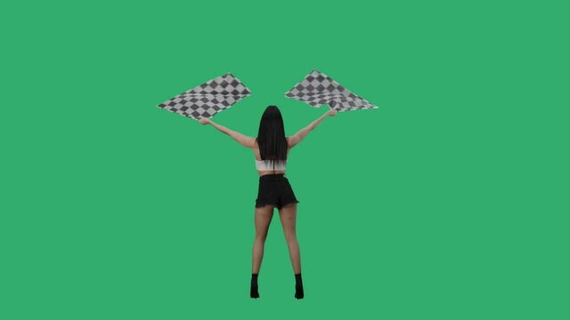 Rear view of sexy brunette in short shorts waving black and white checkered racing flags. Young woman posing full length against background of green screen in studio. Slow motion ready, 4K at 59.94fps