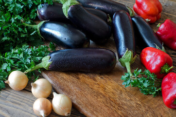 Whole raw eggplant, onions, red bell pepper and parsley on wooden cutting board.