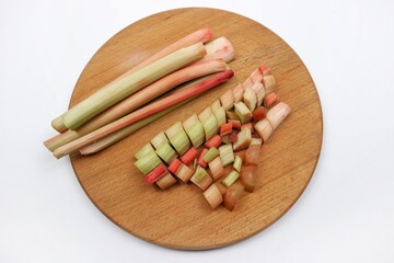 Peeled rhubarb stalks  and rhubarb pieces lie on a wooden cutting board on the white background