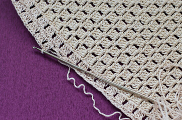 Crocheting with beige cotton threads on a purple background.