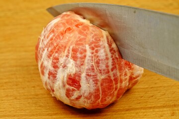 Knife cuts a peeled ripe grapefruit in half on a wooden cutting board