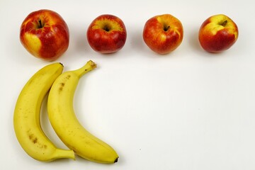 Bananas and red apples lie on a white table 