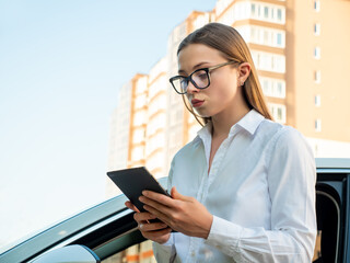 Modern woman businesswoman with a tablet in her hands near her car. 