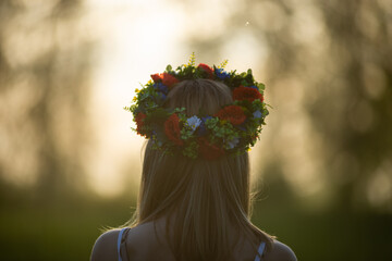 beautiful girl in wreath of flowers in meadow on sunny day. Portrait of Young beautiful woman...