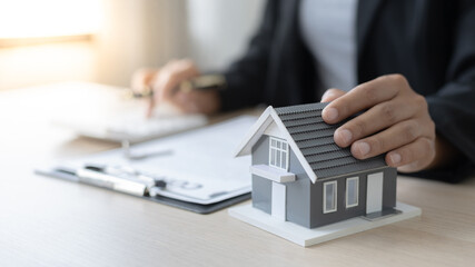 Selling a house with insurance, Salesperson or head of sales holds a model of the house with documentation and calculates the interest-tax-included payment to interested customers.