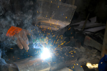 worker welding metal with sparks and smoke in the helmet