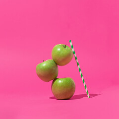 Creative composition with three geen apples and trendy green stripe paper straw on bright pink background. Minimal summer concept with fruit. Healthy life concept.