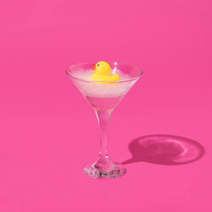 Creative composition with yellow rubber duck and bubble bath foam in martini cocktail glass on bright pink background. Surreal bathing concept. Retro style aesthetic idea.