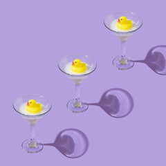 Creative pattern made with yellow rubber duck and bubble bath foam in martini cocktail glass on...