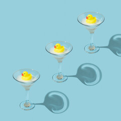 Creative pattern made with yellow rubber duck and bubble bath foam in martini cocktail glass on...