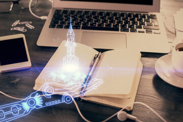 Double exposure of start up theme drawings and desk with open notebook background.