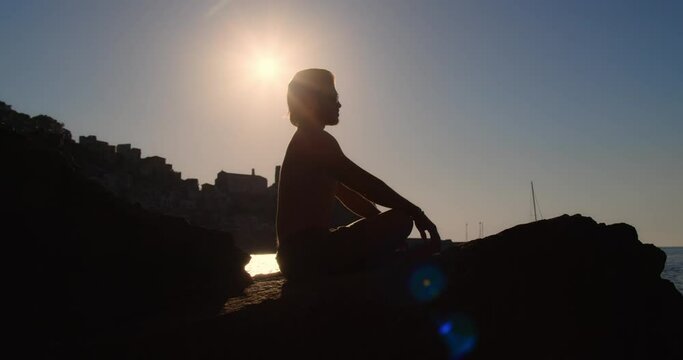 Silhouette di un ragazzo che medita sullo scoglio vicino al mare