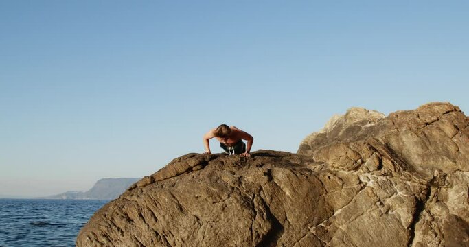 Ragazzo fa allenamento pettorali piegamenti a terra su uno scoglio vicino l'oceano