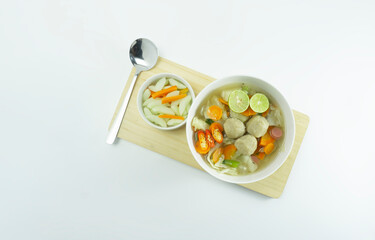 Indonesian Food | Meatball soup served in a white round bowl and pickled carrot cucumber on a white background