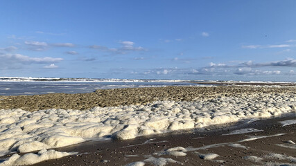 Drift ice and foam on a sandy beach under the cloudy sky © Mike Fortgens/Wirestock