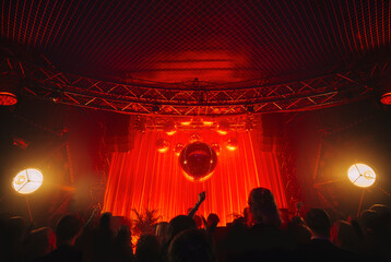 disco ball suspended to the ceiling in the club during the concert, shining with red colour at...